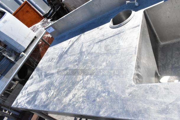 Stainless steel table with sink basin, faucet, and handles, visible surface wear, ideal for commercial kitchen use.