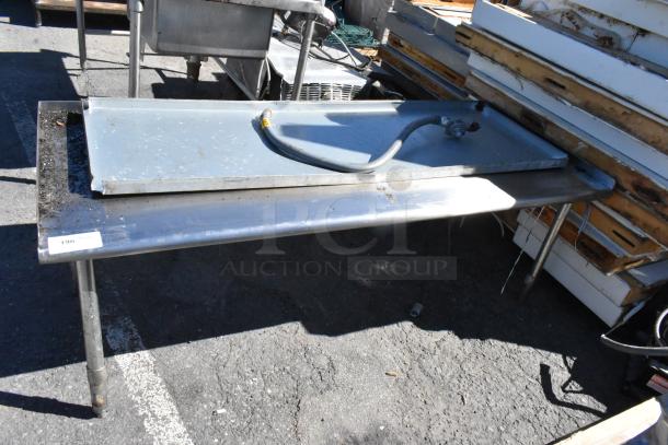 Stainless steel table with attached hose, showing signs of use, item tag 196 visible.