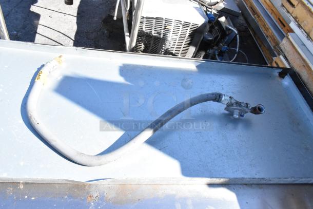 Stainless steel table with visible gas hose attachment, slight surface wear, durable construction, ideal for commercial use.