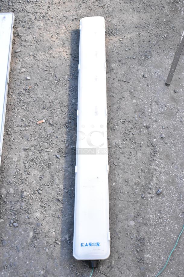 Kason light fixture with a white cover on gravel. Brand logo visible. Durable lighting solution.
