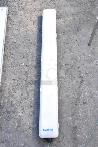 Kason light fixture with a white cover on gravel. Brand logo visible. Durable lighting solution.