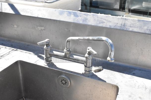 Stainless Steel Table with integrated sink basin, dual-handle faucet, visible wear, includes drawer and under shelf for storage.