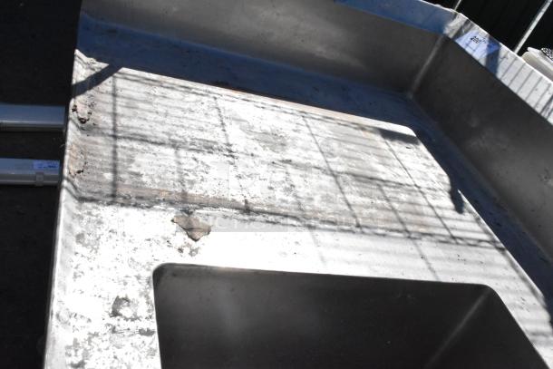 Stainless steel table with sink basin, faucet, handles, drawer, and under shelf; visible wear and rust on surface.
