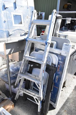 Assortment including metal ladder, folding chairs, and saw horse, showing visible wear, positioned near industrial equipment.