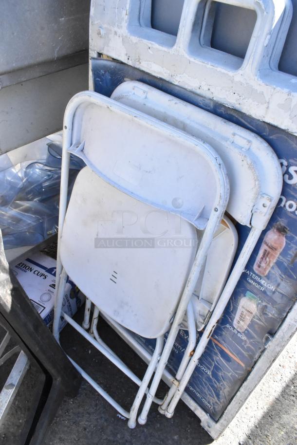 A stack of white folding chairs, visible rust and scratches. Part of a lot including ladder, saw horse, and table. Auction item.