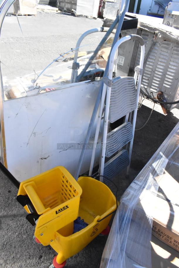Yellow Lavex mop bucket on wheels with caution label, next to a silver 3-step folding ladder. Items are in used condition.