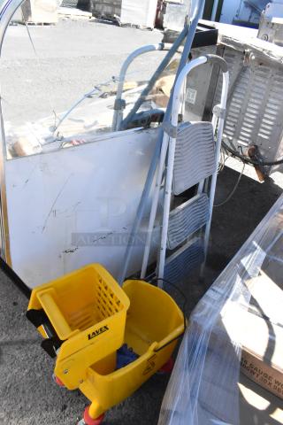 Yellow Lavex mop bucket on wheels with caution label, next to a silver 3-step folding ladder. Items are in used condition.