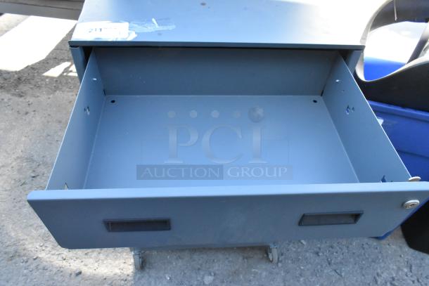 Gray metal cabinet with two drawers; on commercial casters. Open drawer shown; good condition with minor wear.