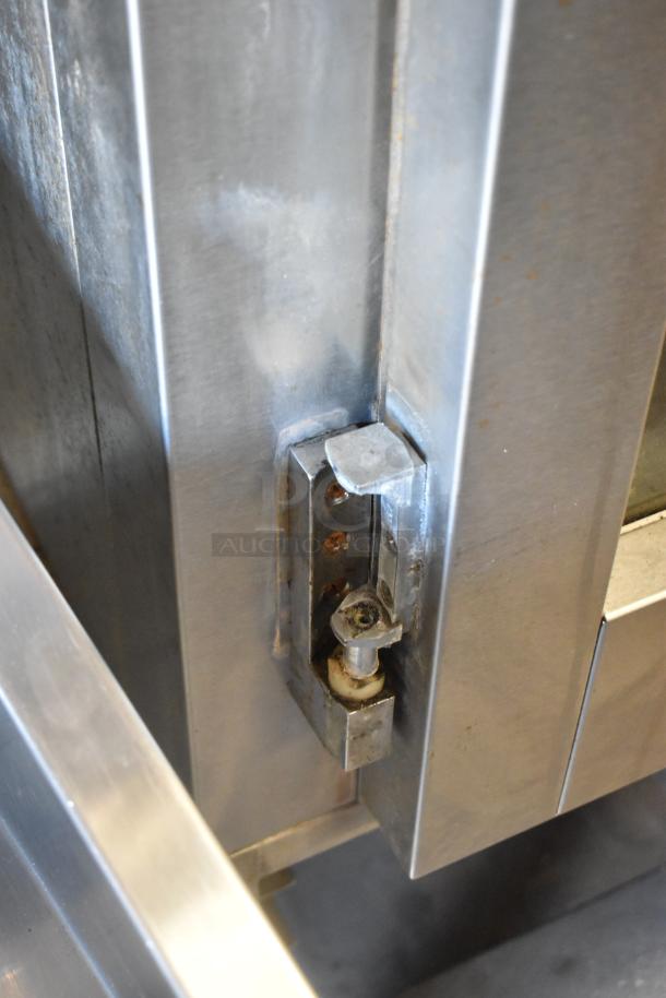 Baxter stainless steel natural gas mini rotating rack oven close-up, showing door latch and steel construction. Some wear visible.