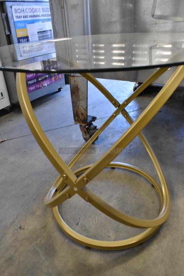 Gold finish table with intersecting legs, circular glass countertop. Modern design, excellent condition, stable base.