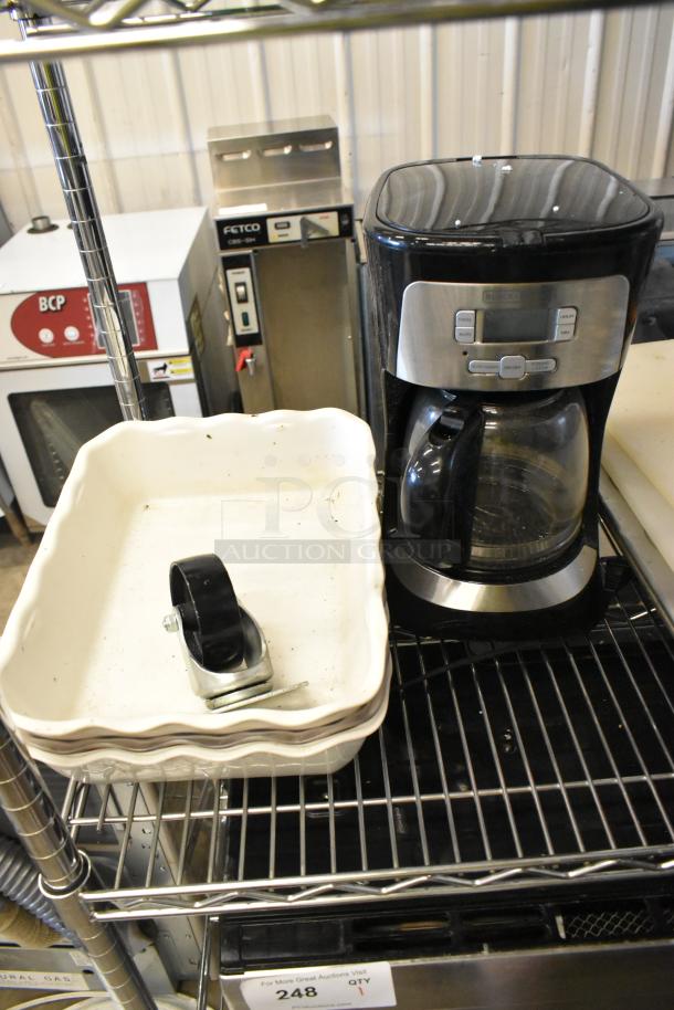 Tier lot featuring various items: black coffee maker, white baking dish with a wheel, on a metal shelf, used condition.