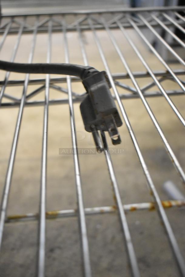 Stainless steel LG LMV1762ST microwave oven resting on a wire shelf with a visible power plug.
