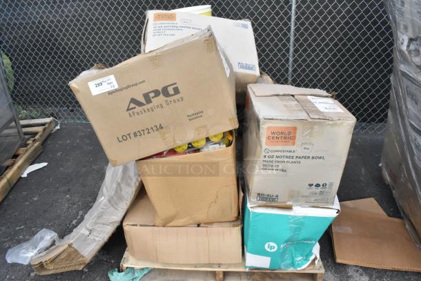 Boxes of scratch and dent items including masking tape, a table lamp, sink, and stoneware plates on a pallet. Labels indicate brand names and item quantities.
