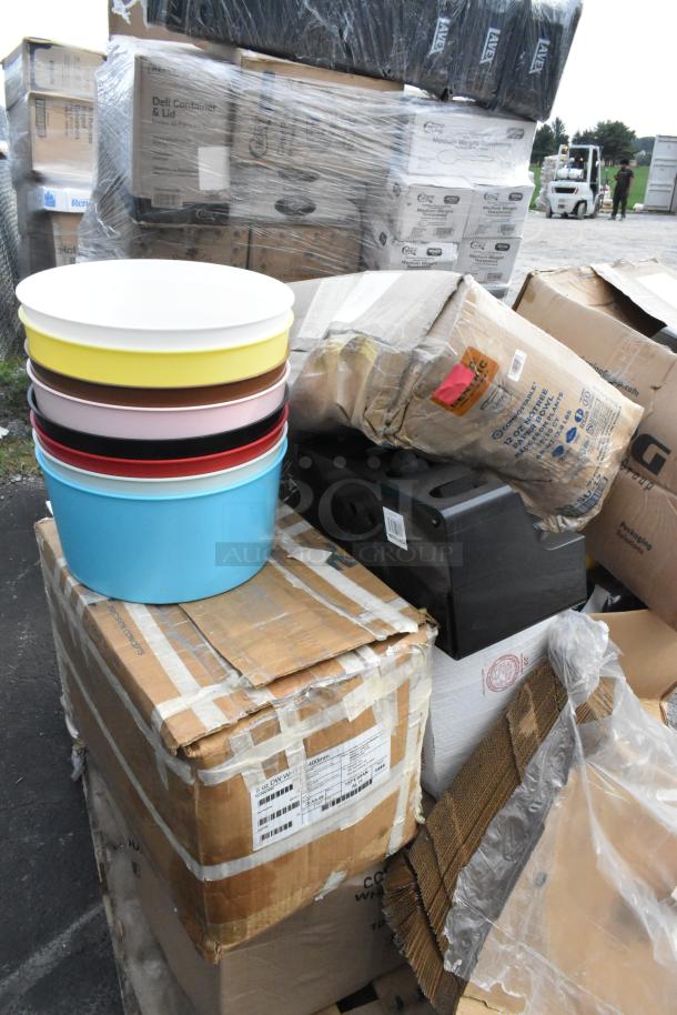 Stack of colorful stoneware plates on a damaged box, surrounded by various sealed packages, indicating a mixed lot auction.