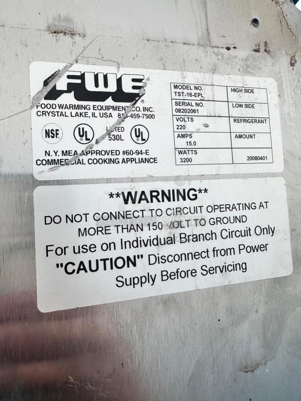 Alt text: "FWE TST-16-EPL Heated Holding Cabinet label showing model, serial number, volts, amps, and safety warnings."