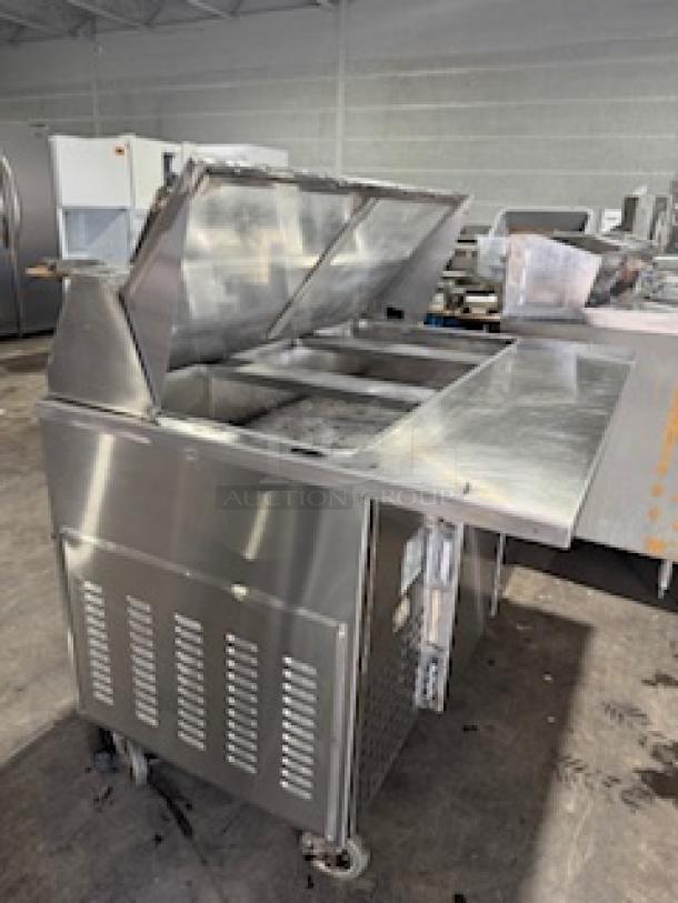 Refrigerated sandwich prep table with clear lid, stainless steel, on casters. Features storage compartments, visible wear.