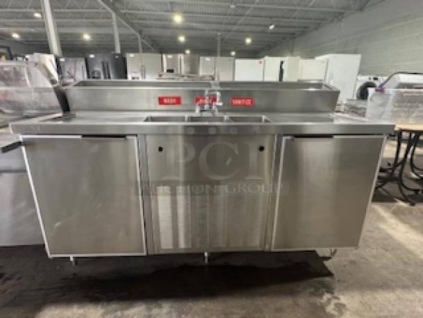 Commercial three-compartment sink with two-door cooler, stainless steel finish, faucet, labeled "HANDWASH" and "SANITIZE."