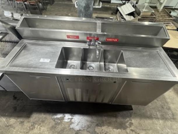 Three-compartment stainless steel sink with attached two-door cooler, ideal for restaurants and bars, in good condition.