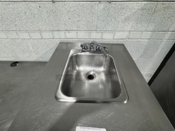 Stainless steel table with single sink, faucet, and backsplash; clean condition, ideal for kitchens or workshops.