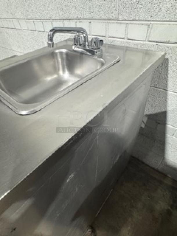 Stainless steel table with single sink and faucet, commercial-grade, minor surface scratches, sturdy construction.
