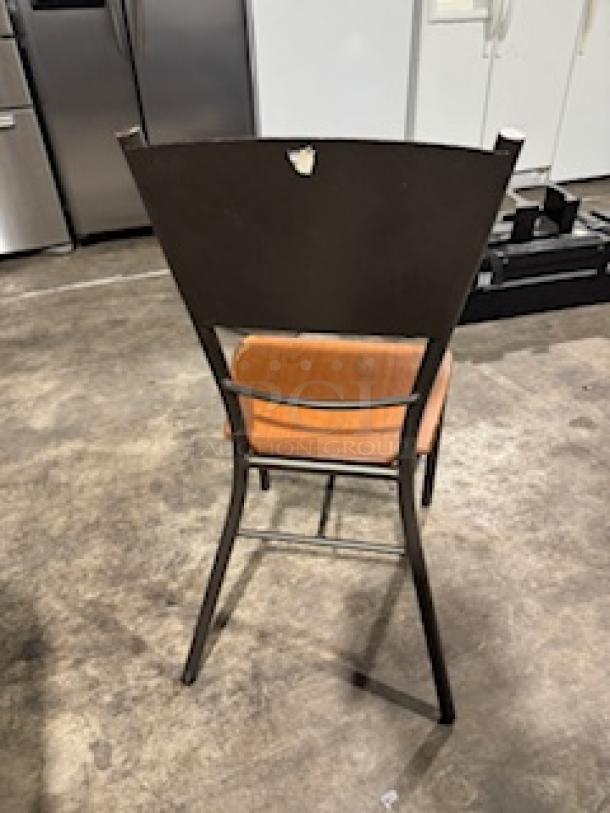 Modern dining chair with bronze metal base, orange cushioned seat, and a dark backrest. Some wear visible.