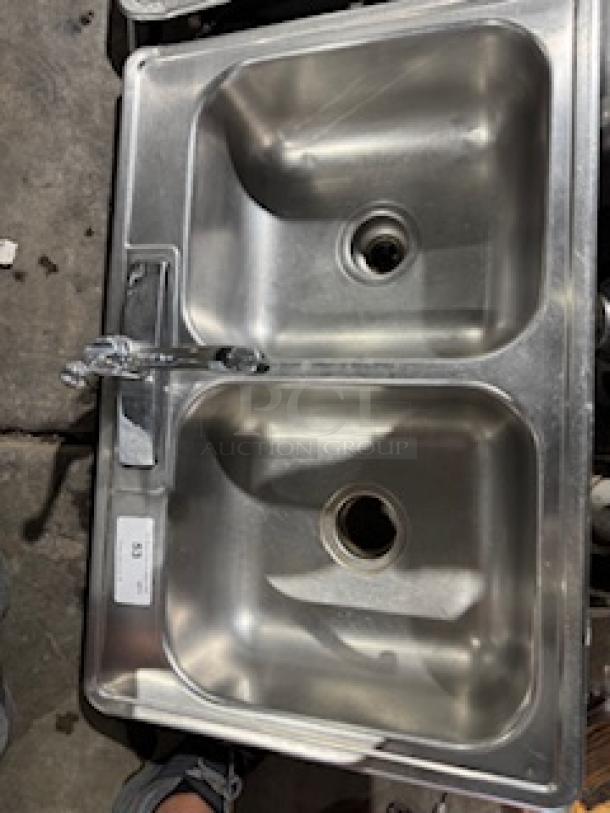 Stainless steel drop-in double sink with faucet, featuring dual basins and central drain openings; gently used condition.
