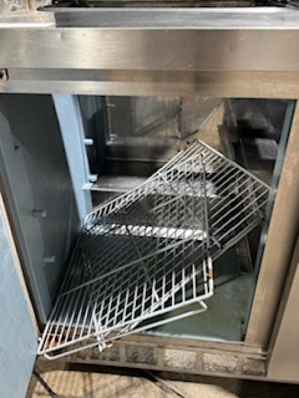 Delfield 4464NP-16 64" refrigerated sandwich prep table, shown open with wire shelves inside, on 3" casters, tested and working.