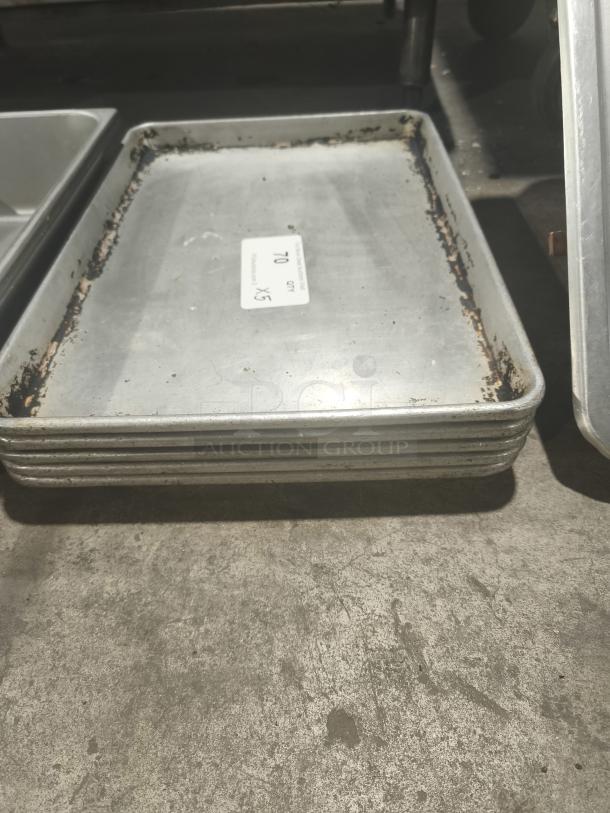 Stack of commercial heavy-duty aluminum half-sheet pans with visible wear, auction tag showing "Lot 70, x5".