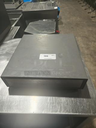 Heavy-duty steel POS cash drawer on metal surface, labeled "104" for auction, showing slight wear, indicating robust construction.