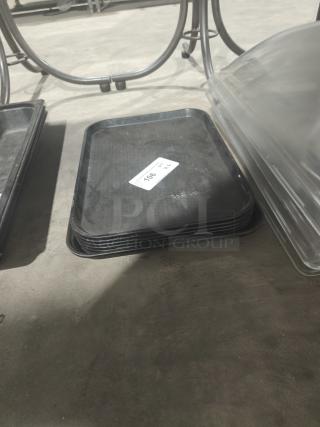 Stack of black commercial plastic cafeteria trays, each 18" x 14", marked with auction number 106. Trays appear in used condition.