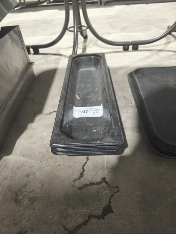 Polycarbonate 1/9-size food pan, black, stackable, viewed from above, auction lot tag with number 107 visible.