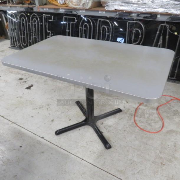 Gray laminate tabletop with black pedestal base, measuring 48x30x30 inches. Slight wear visible, sturdy and functional.