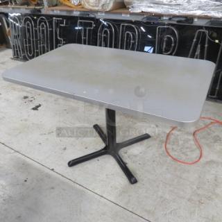 Gray laminate tabletop with black pedestal base, measuring 48x30x30 inches. Slight wear visible, sturdy and functional.