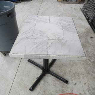 White/gray tile top table with square design on pedestal base, black metal stand; used condition.