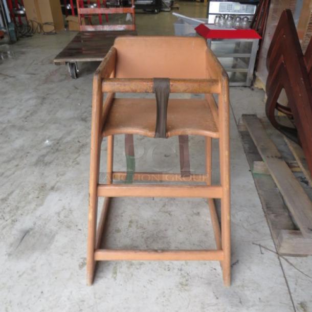 Wooden high chair with brown finish, simple design, and safety strap. Appears in used condition, sturdy and functional.
