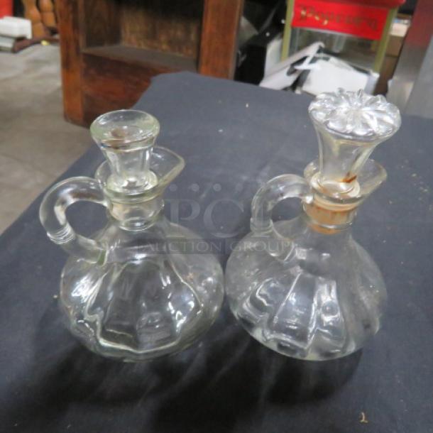 Glass vinegar bottles with stoppers, ribbed design, handle, vintage style. One has a cork stopper. Both in good condition.