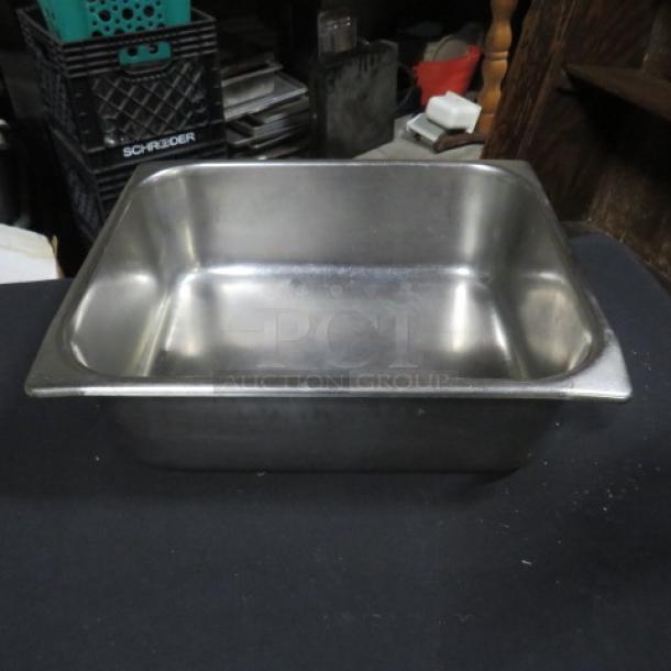 One half size, 4-inch deep stainless steel hotel pan, in used condition, on a dark surface.
