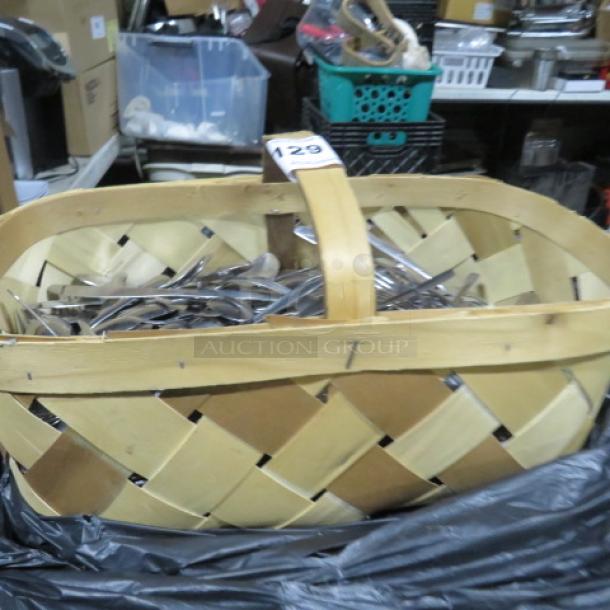Large woven basket filled with assorted flatware, including forks, spoons, and knives. Numbered tag on handle, indicating lot 129.