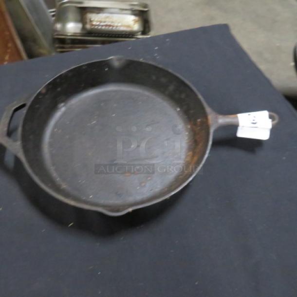 12-inch cast iron skillet with visible wear. Features dual pour spouts and a handle hole. Auction tag attached to handle.