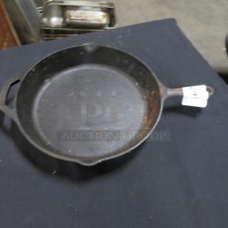 12-inch cast iron skillet with visible wear. Features dual pour spouts and a handle hole. Auction tag attached to handle.