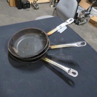 Three stacked 8.5-inch sauté pans with long handles, showing signs of wear and discoloration. Tag labeled "69" attached.