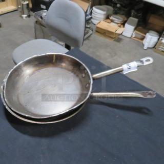 Two stacked 12-inch sauté pans with long handles, showing signs of use. Auction tag "69" attached to handle.
