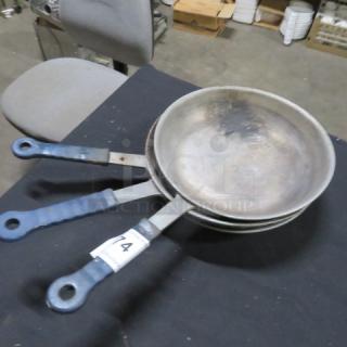 Three 10-inch sauté pans with Kool Touch handles, showing signs of use. Tag marked "74" attached to one handle.