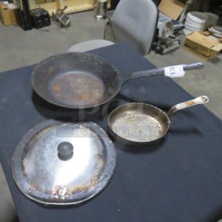 Lot of miscellaneous cookware items including two frying pans and a lid; showing visible wear and rust.