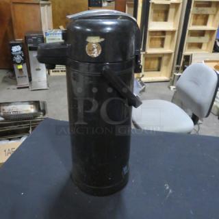 Black airpot with pump lid, handle, and worn label. Used condition with visible scratches. Ideal for coffee dispensing.
