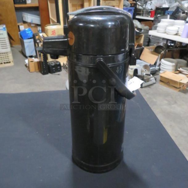 Black airpot with handle and spout, used condition. Upper side label visible, indicating contents or instructions.