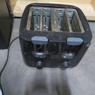 Black 4-slice toaster with adjustable settings, showing some wear. Power cord attached. No visible brand or model details.