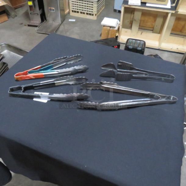 Assorted kitchen tongs on a table, featuring metal and rubber grips, shown in good condition.