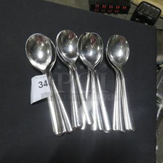 Set of 24 stainless steel serving spoons, gently used condition, reflective finish, stacked in a lot, auction tag visible.