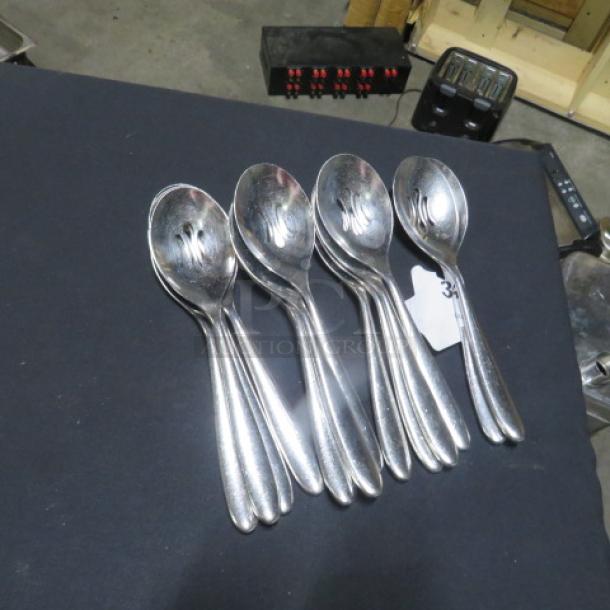 One lot of 14 silver slotted spoons on display, excellent condition, set of five shown.